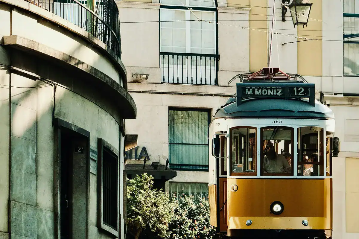 Historische gelbe Strassenbahn faehrt durch eine enge Gasse in Lissabon